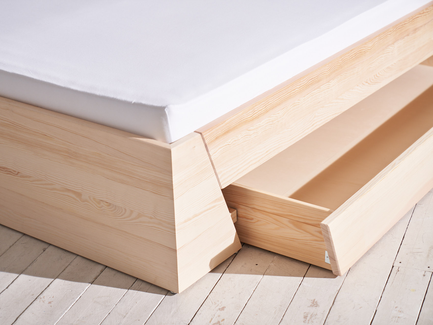 Massivholz Stauraumbett Schublade geöffnet schräge Ansicht auf weißem Holzboden Nahaufnahme