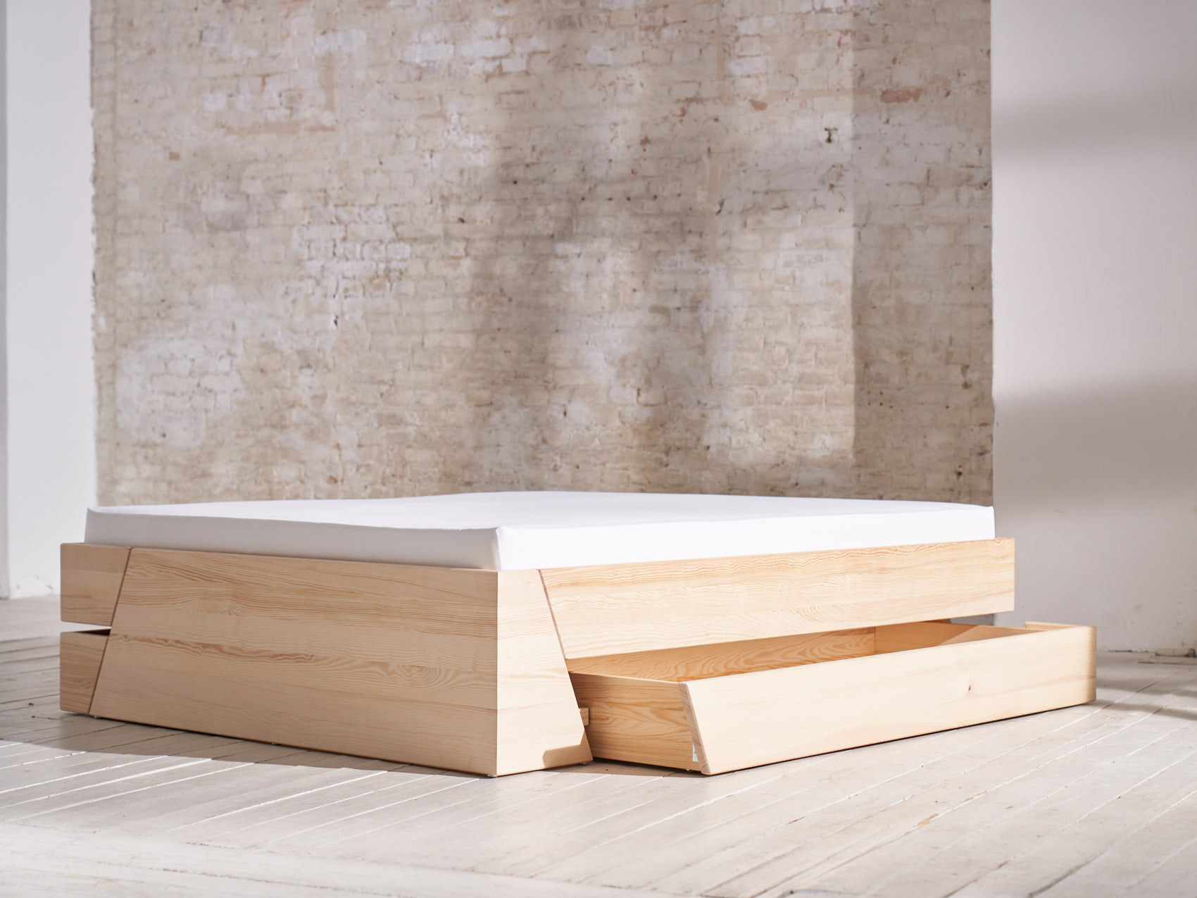 Massivholz Stauraumbett Schublade offen auf weißem Holzboden vor heller Backsteinwand