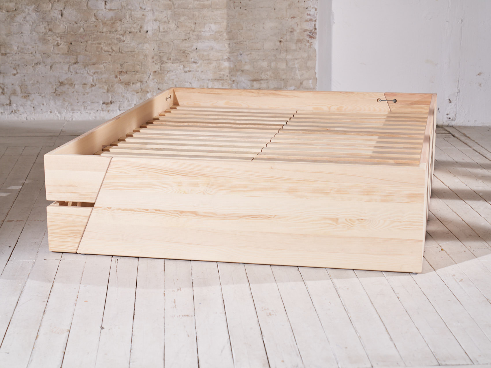Massivholz Stauraumbett ohne Matratze Lattenrost auf weißem Holzboden vor heller Backsteinwand