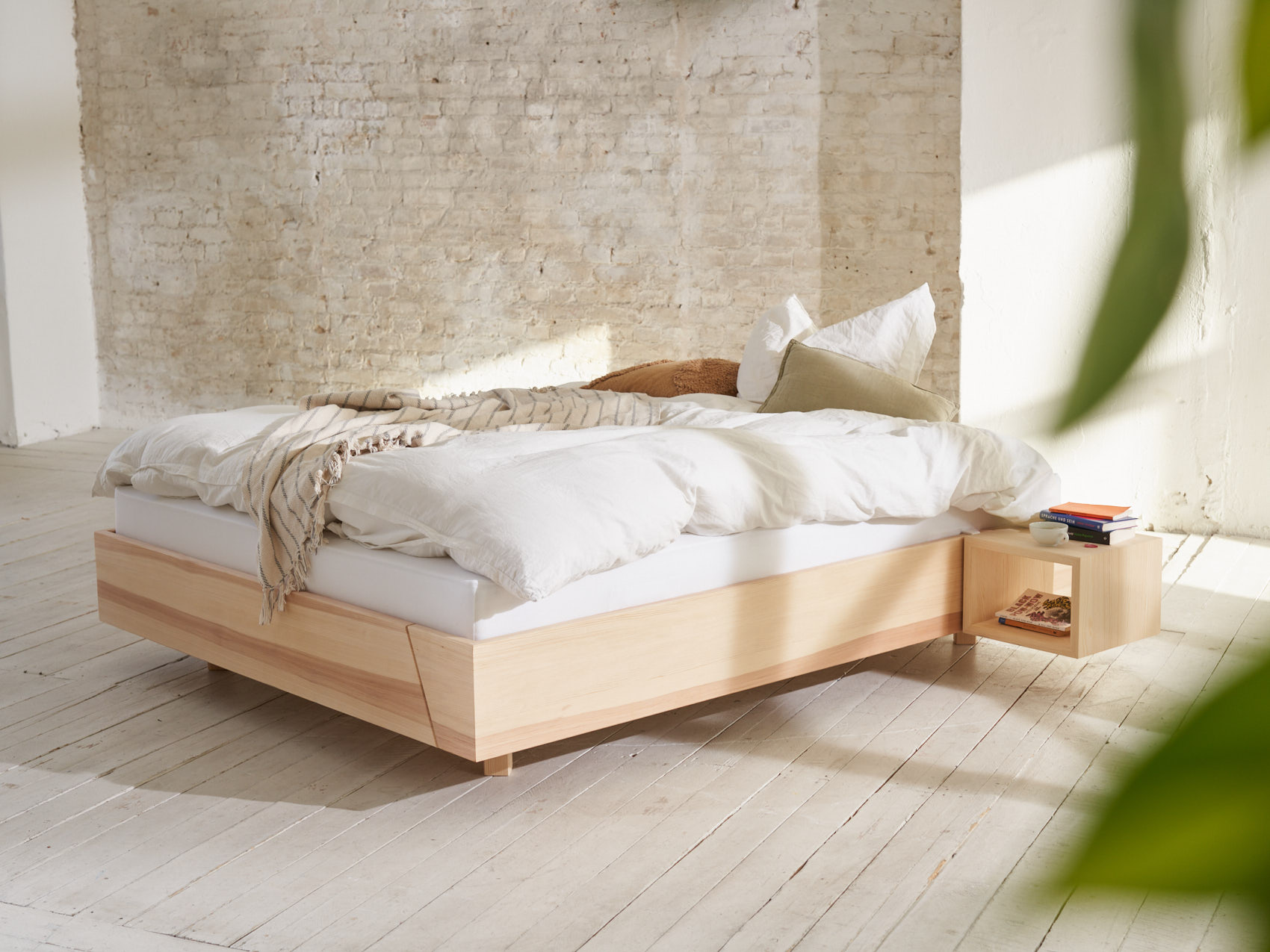 Massivholzbett schwebend Kiezbett im Raum Blätter im Vordergrund