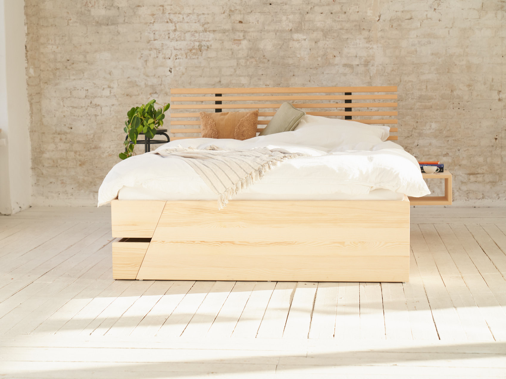Massivholz Stauraumbett Kiezbett Schlafzimmer belebt im Raum auf Holzboden vor heller Backsteinwand