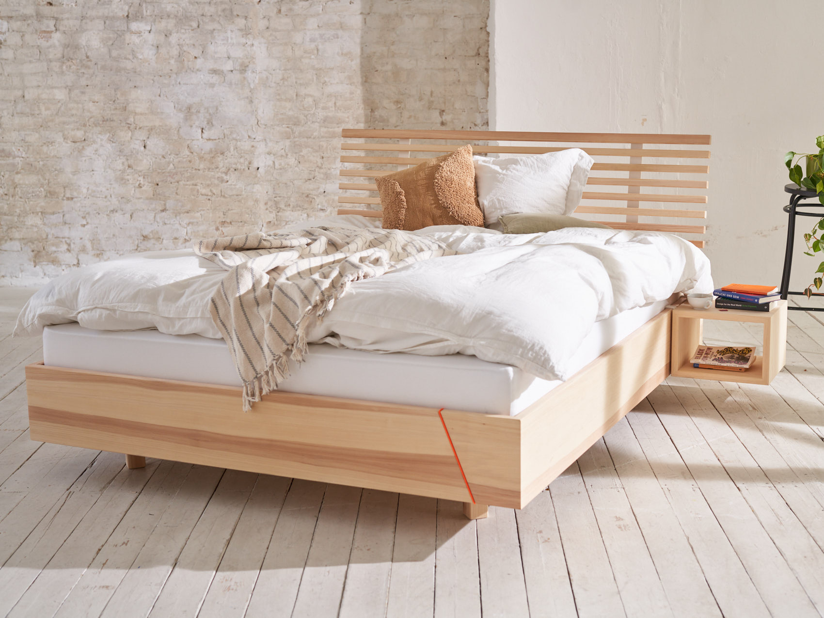 Massivholzbett kiezbett schwebend Schlafzimmer belebt auf weißem Holzboden vor heller Backsteinwand